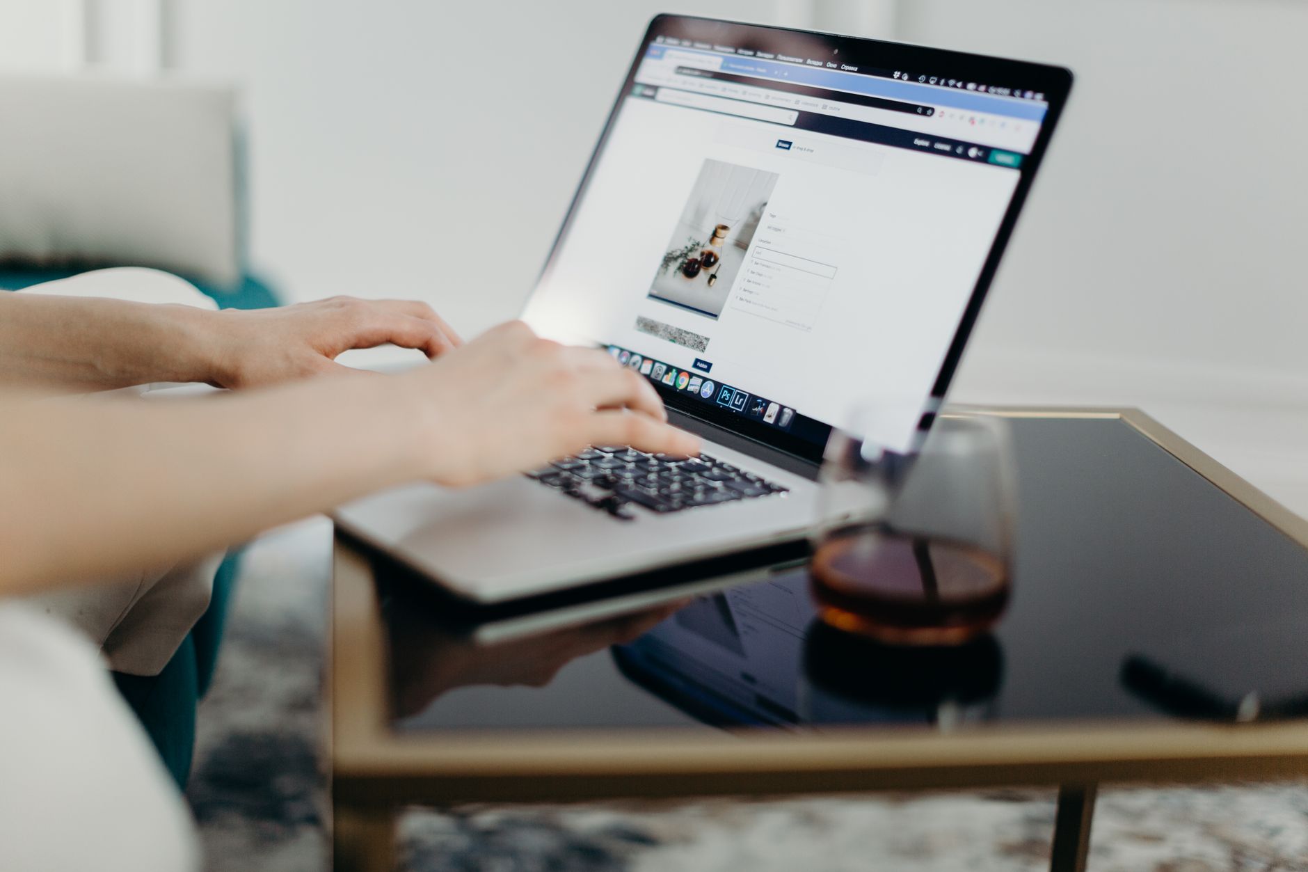 Mani che digitano su un portatile appoggiato su un tavolino di vetro, con un bicchiere accanto